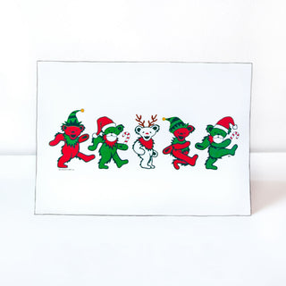 A horizontal white greeting card with a line of five Grateful Dead dancing bears: a red bear with a green elf hat, a green bear with a white beard and red Santa hat, a white bear with red reindeer antlers, followed by another red bear and another green bear.